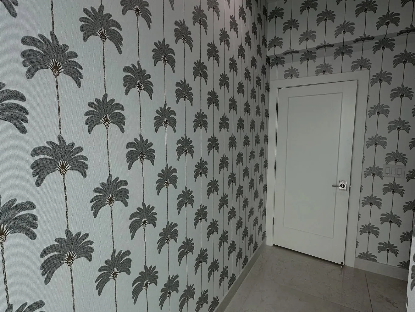 During the wallpaper repair stage, an installer uses a fine-tip adhesive syringe to place paste behind a lifted seam while holding the paper flat with the other hand
